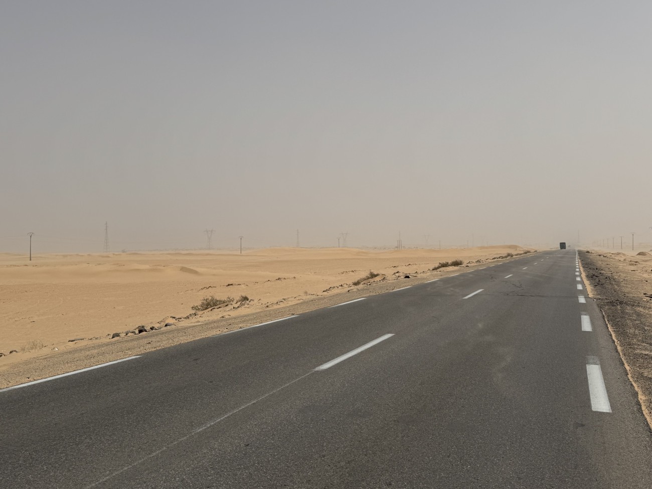 A road with sand and dust to the sides. Various cables are running alongside the road