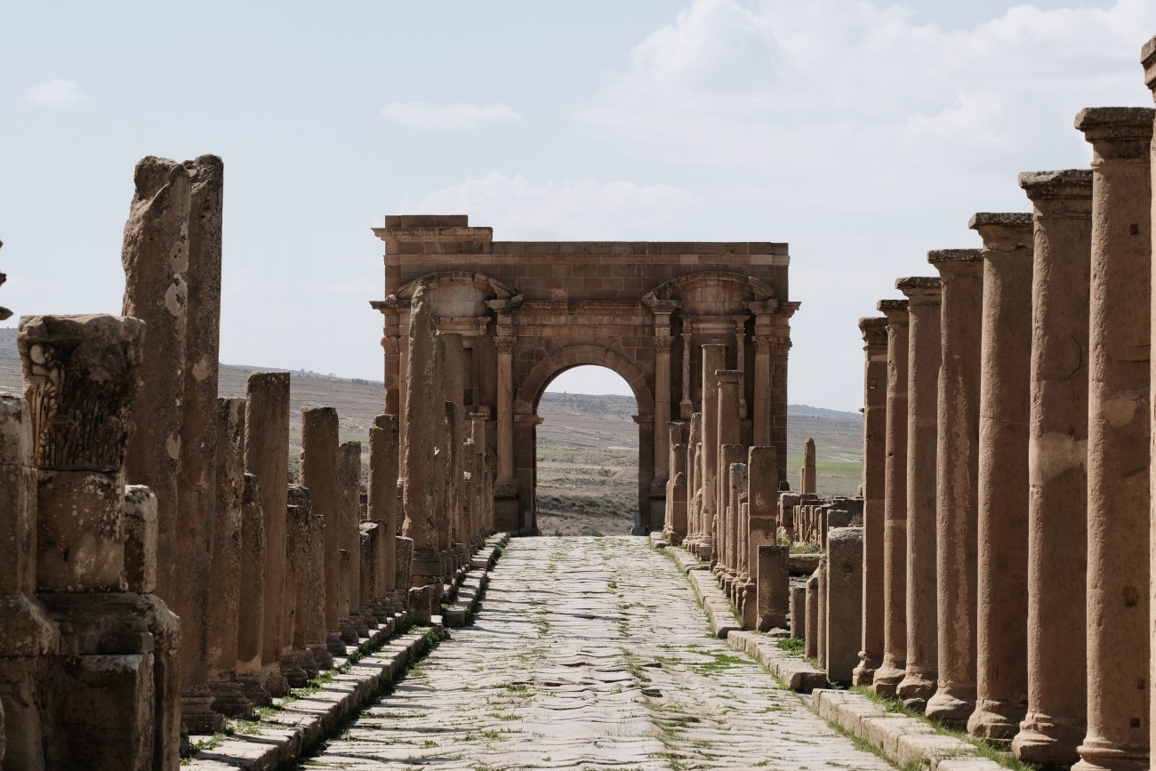 A roman road, flanked by columns, leading to an archway