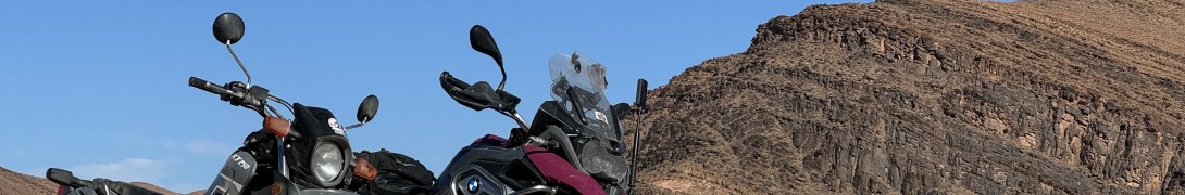 Our two motorcycles, a BMW GS and a Yamaha XT250, parked in the oued with a rough ground and mountains behind